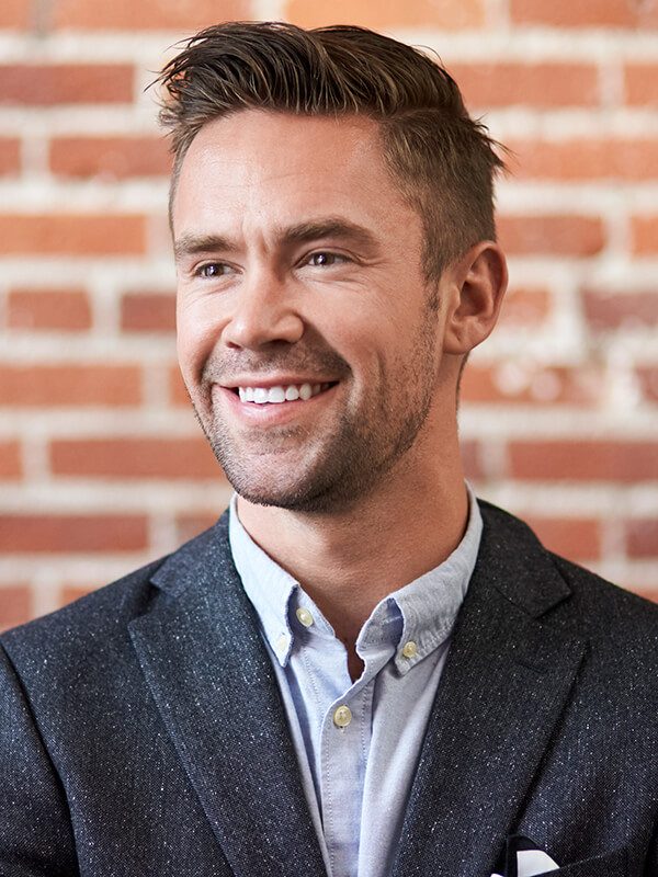 young-businessman-standing-against-brick-wall-in-m-D2ZSHCQ