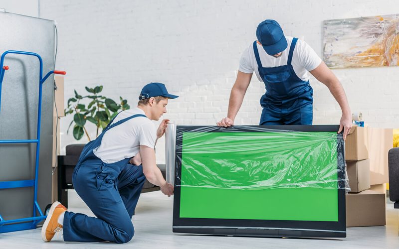 two-movers-in-uniform-using-roll-of-stretch-film-56UCF9E