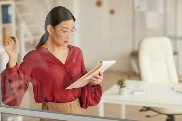 asian-businesswoman-writing-on-glass-in-office-7ZXYVHY
