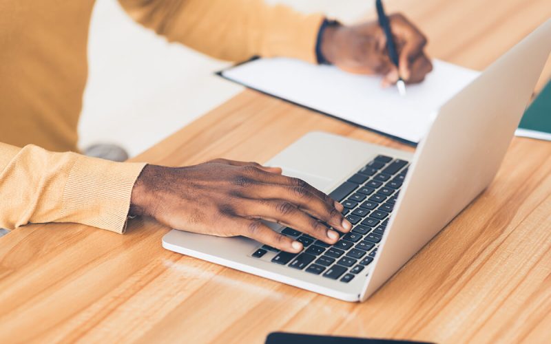 unrecognizable-black-guy-working-on-his-laptop-RF6ZCJQ